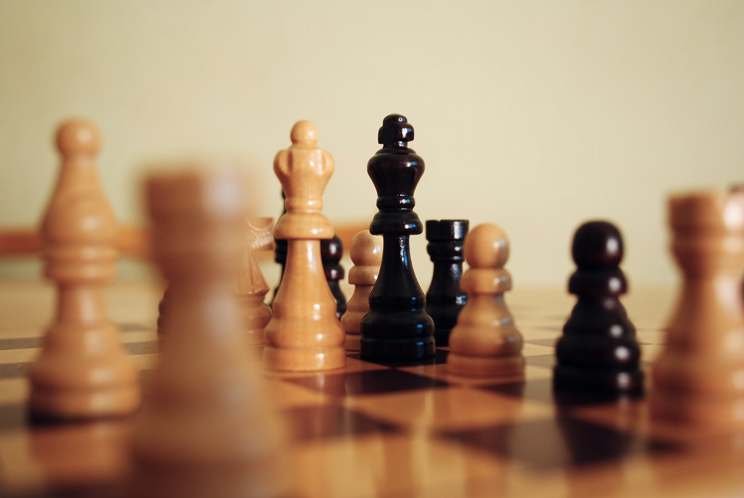 Chess board with wooden pieces in play, black king in focus surrounded by light and dark pieces on wooden board.