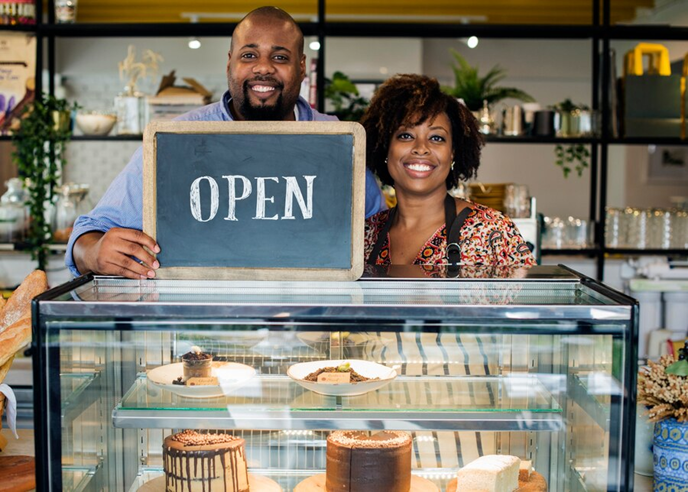 Business owners proudly standing with an open sign for their shop.