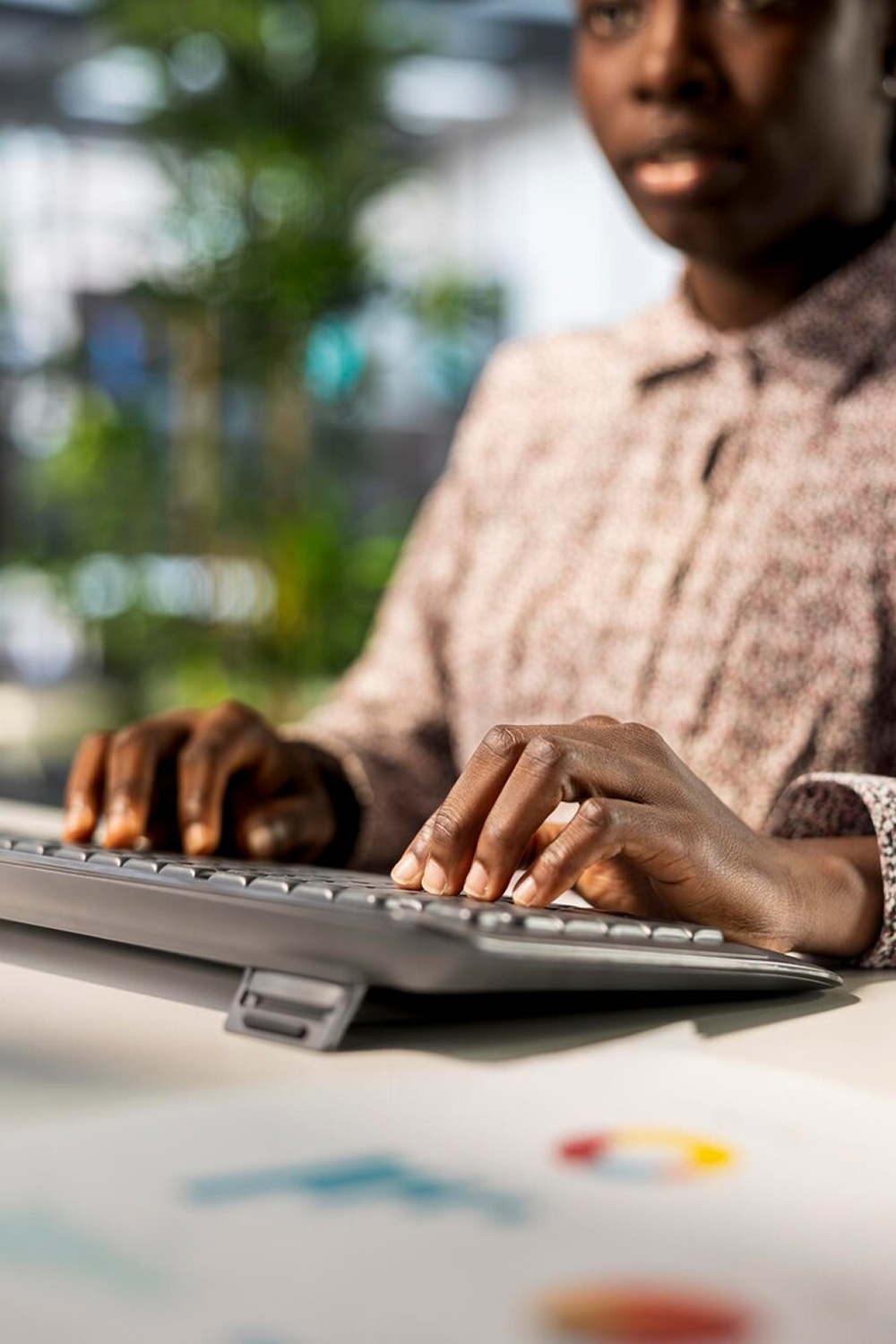 Support person typing on laptop keyboard, ready to help, with office background and documents on desk.